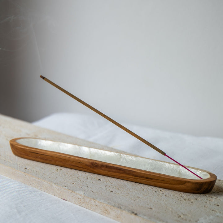 Wooden incense holder with a single red incense stick on a light surface.