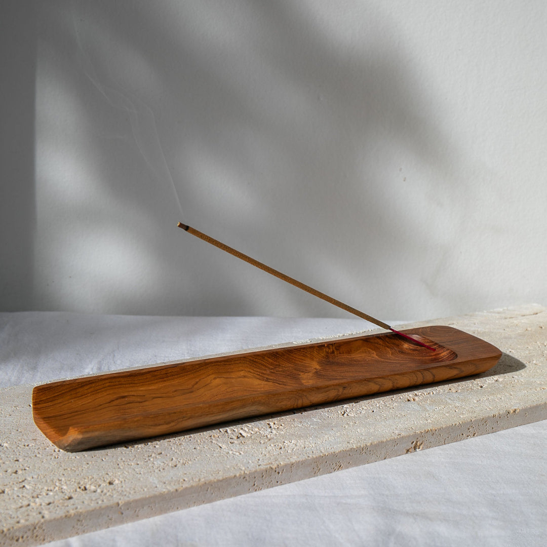 Wooden incense burner with a single incense stick on a light surface with a neutral background