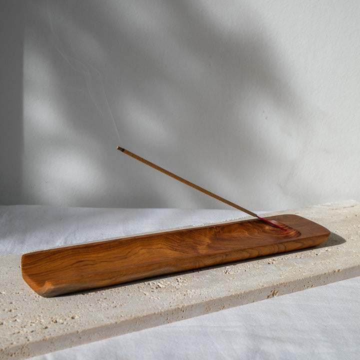 Wooden incense burner with a single incense stick on a light surface with a neutral background